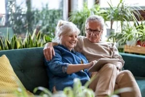 An older man and woman sit together on a couch looking at common reasons why people move to retirement communities.