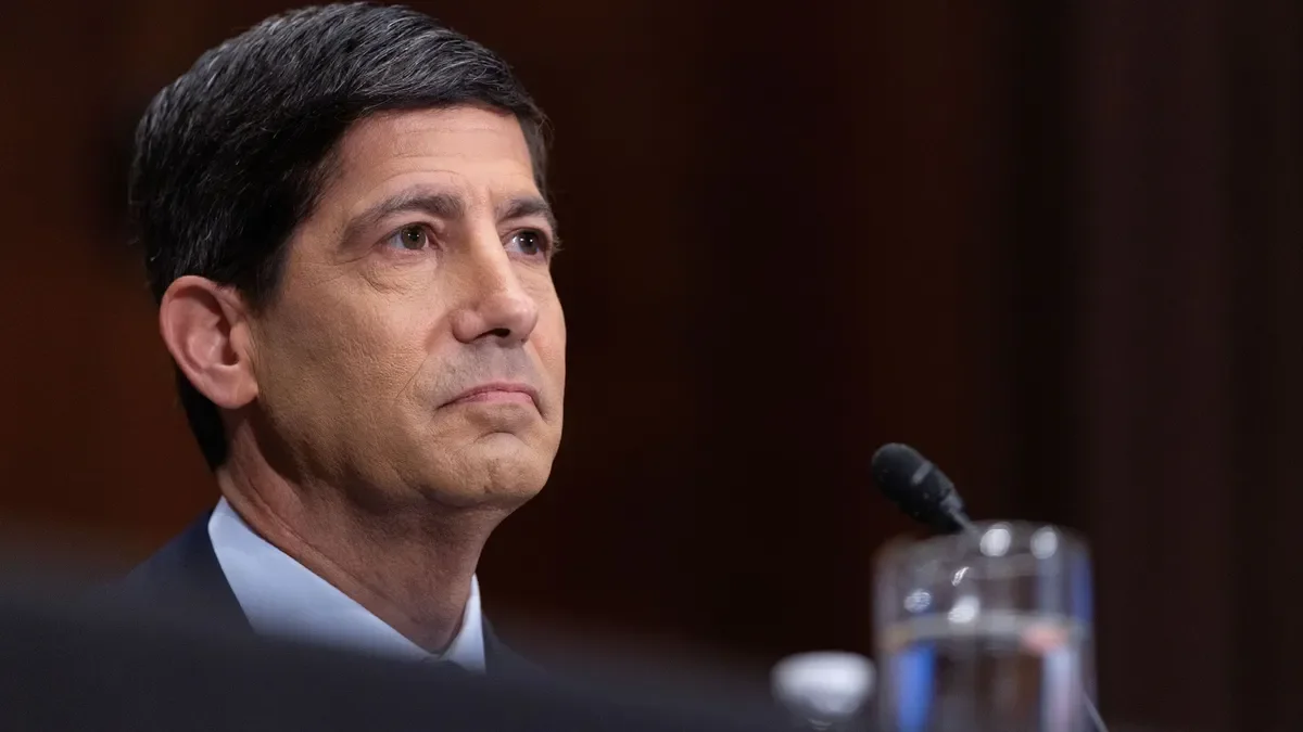 A close-up of a person wearing a suit and tie, listening during a committee hearing.